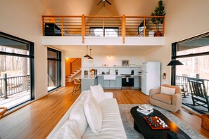 A spacious loft with a high ceiling, a kitchen, a dining area, and a cozy seating area with a sofa and armchairs.