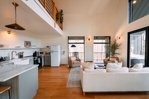 A modern kitchen with a central island, a dining area with a sofa, and a view of the outdoors through large windows.