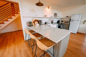 A modern kitchen with a central island, bar stools, a microwave, a refrigerator, and a wooden staircase.