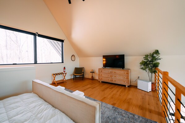 A bedroom with a bed, a dresser, a television, a chair, and a window.