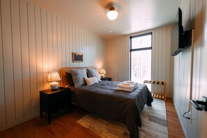 A bedroom with a bed, bedside lamps, a picture on the wall, and a window.