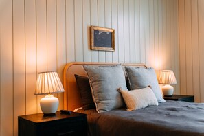 A neatly made bed with a headboard, two bedside lamps, and a framed picture on the wall.