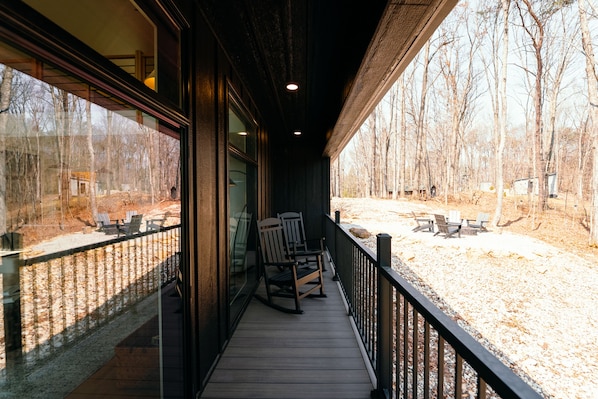 A wooden deck with chairs and tables, overlooking a forested area.
