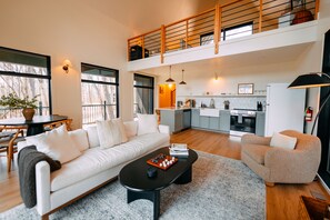 A spacious living area with a sofa, coffee table, and a dining table. A kitchen is visible in the background with modern appliances. - Stonehaven | Hocking Hills, Modern, Views, Hot Tub (Rockbridge)
