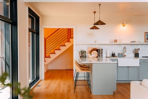 A modern kitchen with a central island, wooden flooring, and a staircase leading to another level.