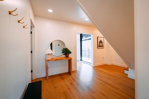 A hallway with wooden flooring, a mirror, a lamp, a potted plant, and a framed picture on the wall. - Stonehaven | Hocking Hills, Modern, Views, Hot Tub (Rockbridge)