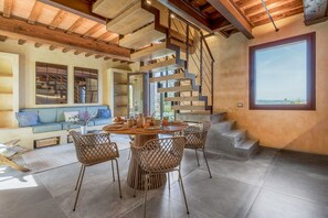 A modern interior with a wooden staircase, a round dining table, and a large window offering a view.