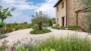 A stone building with a gravel driveway and a variety of plants and flowers. - Punteriolo Family Apartment, Nice Garden, Pool (Montaione)