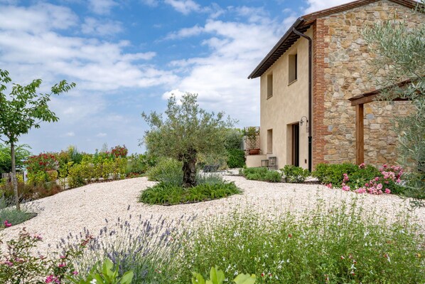 A stone building with a gravel driveway and a variety of plants and flowers.