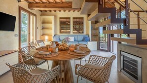 A modern dining area with a round wooden table, wicker chairs, and a built-in fireplace. - Punteriolo Family Apartment, Nice Garden, Pool (Montaione)