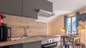 A modern kitchen with a built-in stove, a sink, and a dining area with a table and chairs. - Le Petit Aravis - panoramic balcony and village (La Giettaz)