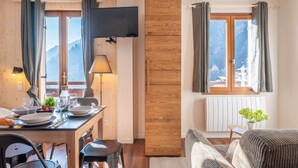 A cozy room with a wooden dining table set for two, a sofa, and a window with curtains. - Le Petit Aravis - panoramic balcony and village (La Giettaz)