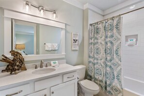 A bathroom with a white sink, mirror, and toilet. There is a patterned shower curtain and a towel rack with a towel.