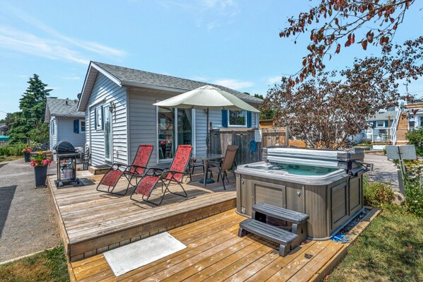 A deck with a hot tub, lounge chairs, and a barbecue grill. - West Lake Cottage at The Birch (Prince Edward)