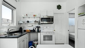 Une cuisine de taille réduite avec des meubles blancs, un four à micro-ondes, une cuisinière et un évier.