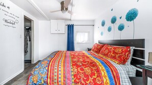 Una camera da letto con un letto grande, un ventilatore a soffitto, un armadio e una finestra con tende blu.