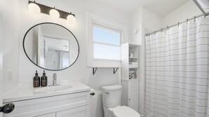 A bathroom with a white vanity, a round mirror, a toilet, and a shower curtain.