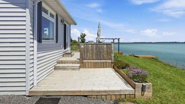 A waterfront mobile home with a wooden deck, a pergola with an umbrella, and a view of the water.