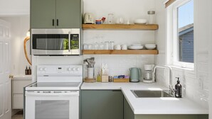 A compact kitchen with a microwave, stove, and coffee maker, along with a window providing natural light. - Wellington Cottage at Twin Birch Suites (Prince Edward)