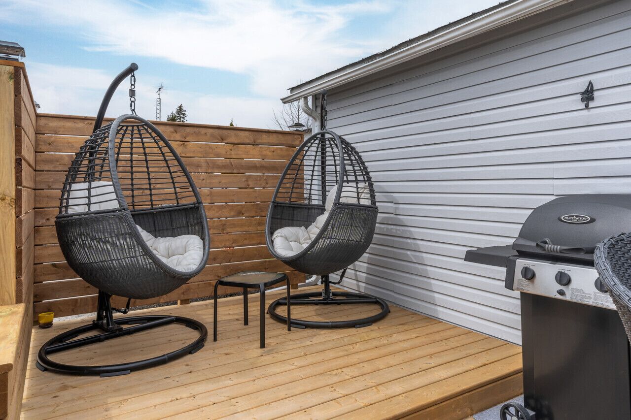 Deux chaises suspendues sur une terrasse en bois, un barbecue et une clôture en bois.