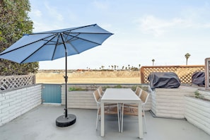 Relax on the patio with a shaded table and chairs overlooking the beach and palm trees.