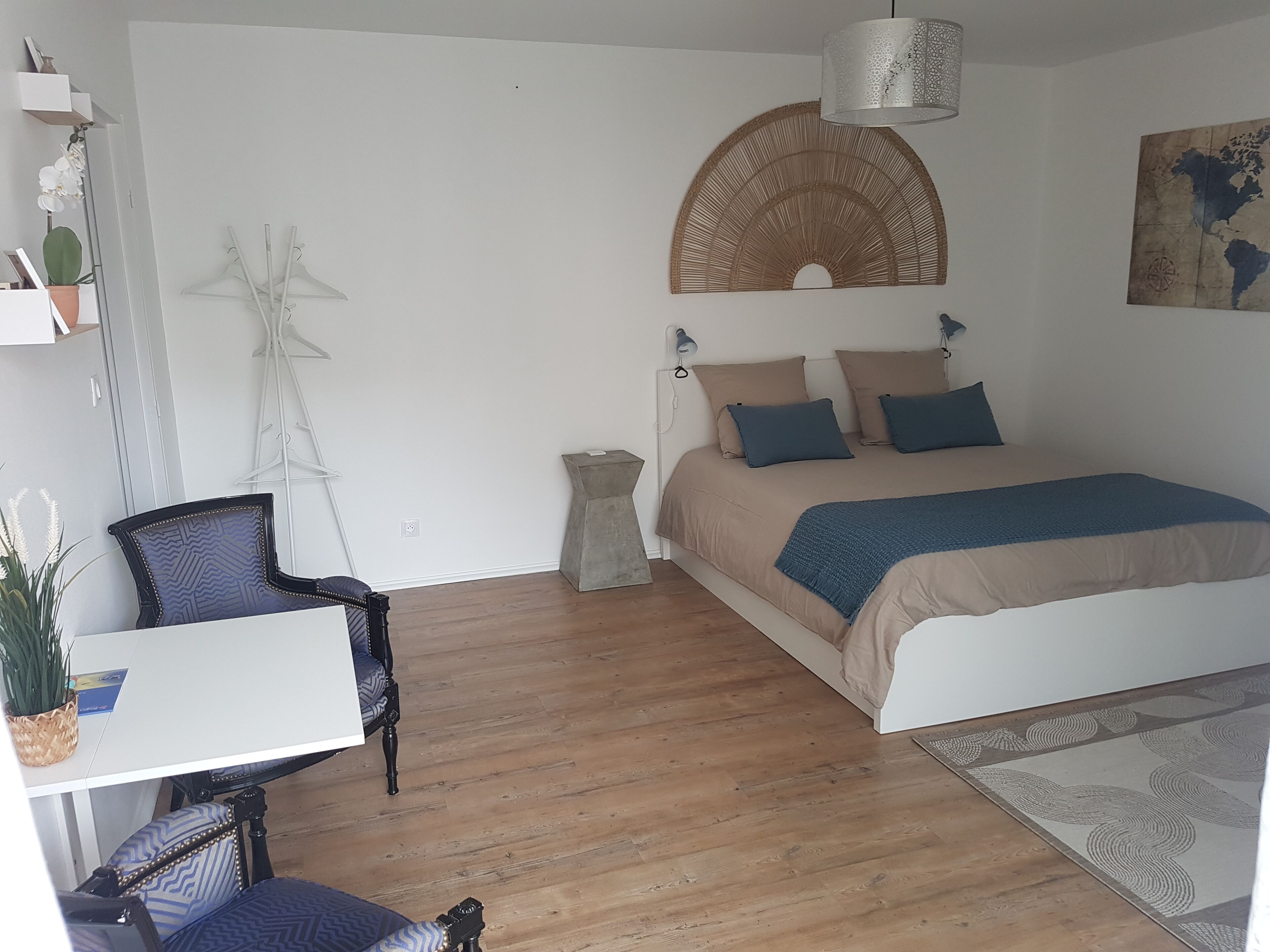 A bedroom with a bed, a chair, a small table, a hanging light fixture, and a world map on the wall.