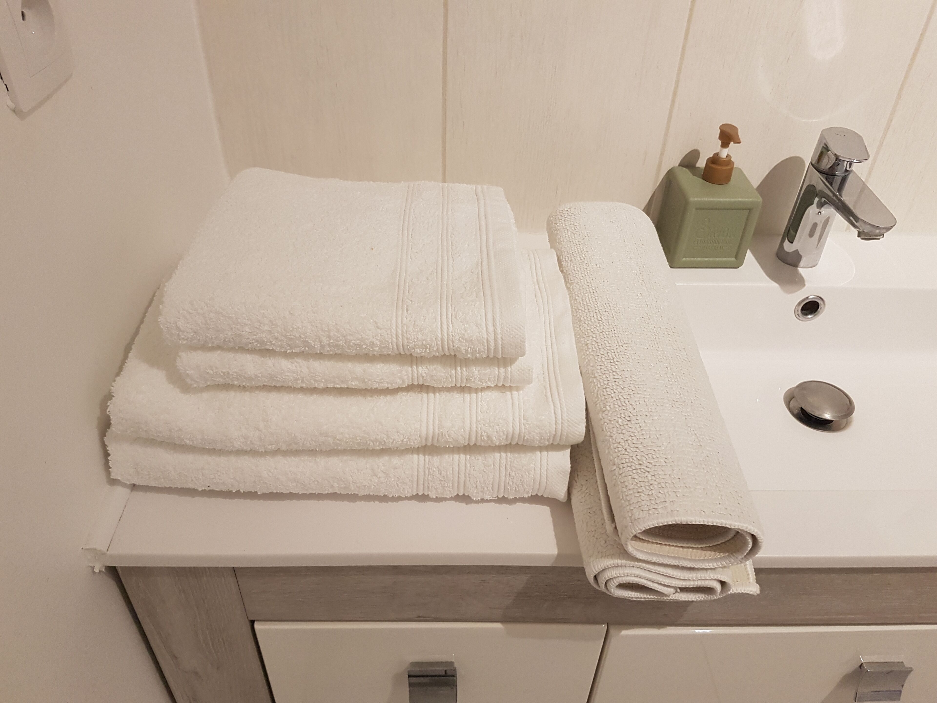 Ein Badezimmer mit einem weißen Waschbecken, einem Spiegel und einem Stapel weißer Handtücher.