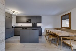 A modern kitchen with a central island, dark cabinetry, and a wooden dining table with chairs. - Ground floor, view lake, balcony, tv, ski locker, 56m², Tignes (Tignes)