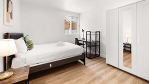 A bedroom with a bed, bedside table, lamp, and a wardrobe. - Urban Retreat USC (Los Angeles)