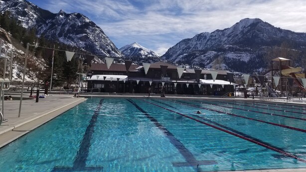 A swimming pool with clear blue water, surrounded by mountains and a building with a sloped roof. - Charming Historic Bungalow (Montrose)