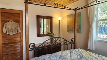 Un dormitorio con una cama con dosel, una puerta de madera, un espejo, una lámpara de pie y una ventana con cortinas.