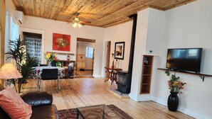 A spacious living room with a wooden ceiling, a fireplace, a television mounted on the wall, and a dining area with a table and chairs. - Charming Historic Bungalow (Montrose)
