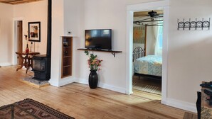 A room with a wooden ceiling, a TV on a shelf, a bed with a patterned bedspread, and a small table with a vase of flowers. - Charming Historic Bungalow (Montrose)