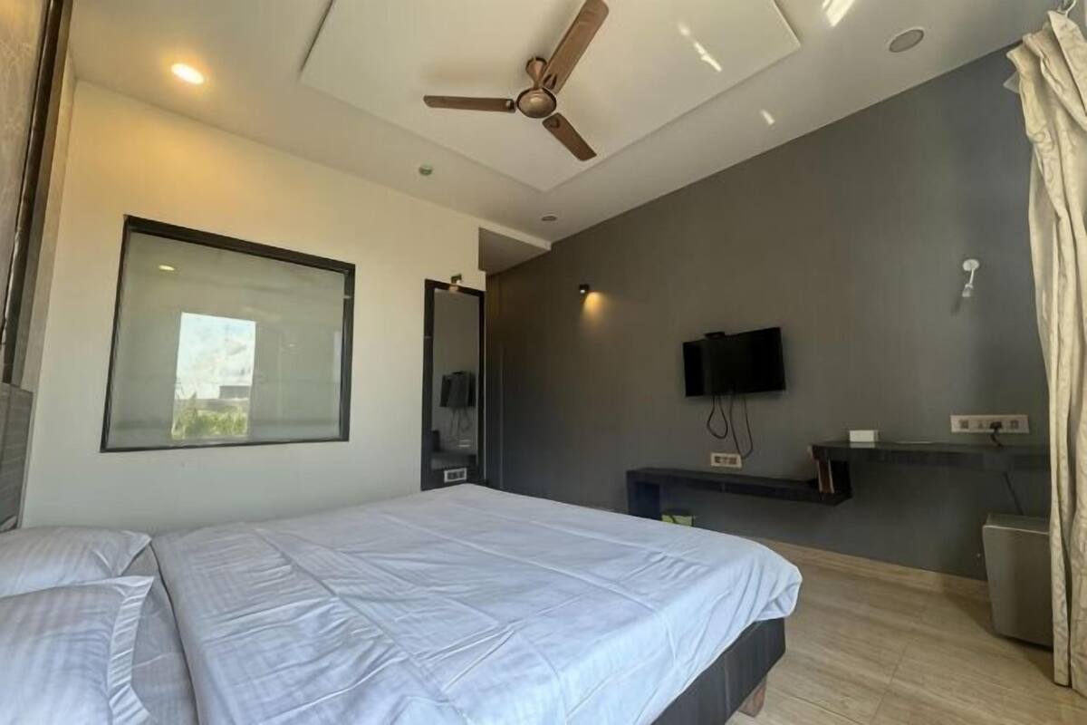 Een moderne slaapkamer met een bed, plafondventilator, televisie en een raam.