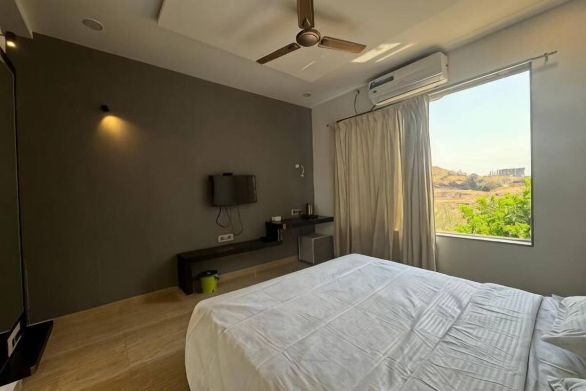 Een slaapkamer met een bed, een plafondventilator, een televisie, een raam met gordijnen en uitzicht op een landschap.