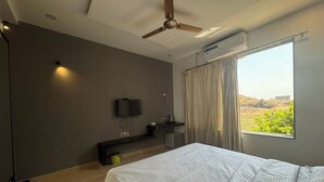 Une chambre moderne équipée d’un lit, d’un ventilateur de plafond, d’un climatiseur, d’un téléviseur fixé au mur et d’une fenêtre avec des rideaux.
