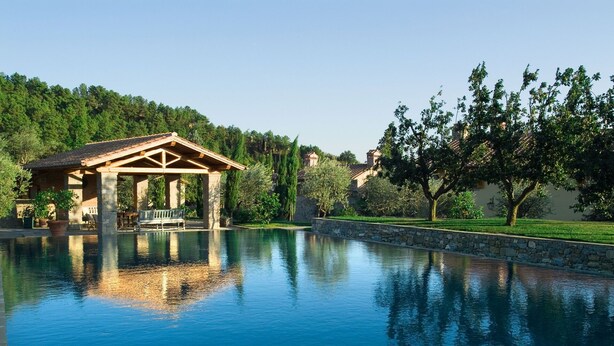 A serene pool area with a gazebo, stone walls, and lush greenery.