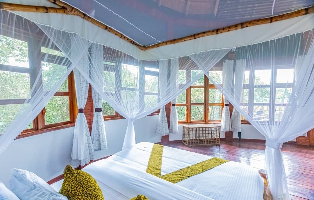A room with a bed, white curtains, and large windows.