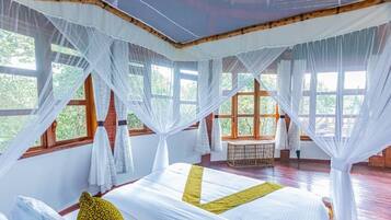 A room with a bed, white curtains, and large windows.