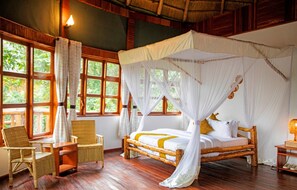 Ein Zimmer mit einem hölzernen Bett, einem weißen Baldachin, Korbstühlen und großen Fenstern.