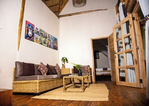 A cozy living room with a wicker sofa, a small coffee table, and a wall adorned with a colorful poster. - Kibale Tourist Safari Lodge (Kibale)