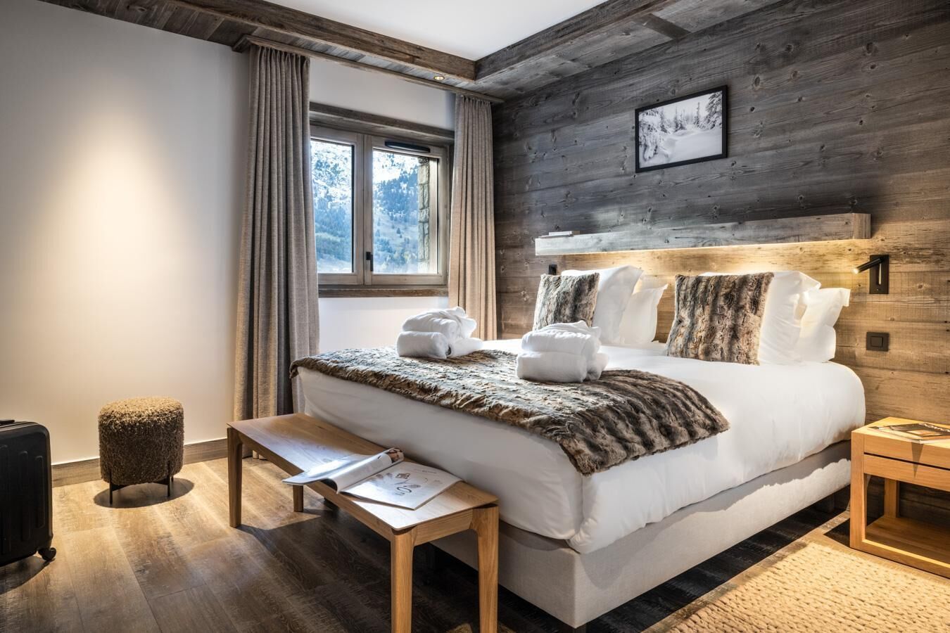 Een moderne slaapkamer met een groot bed, een houten hoofdbord en uitzicht op een besneeerd landschap door het raam.