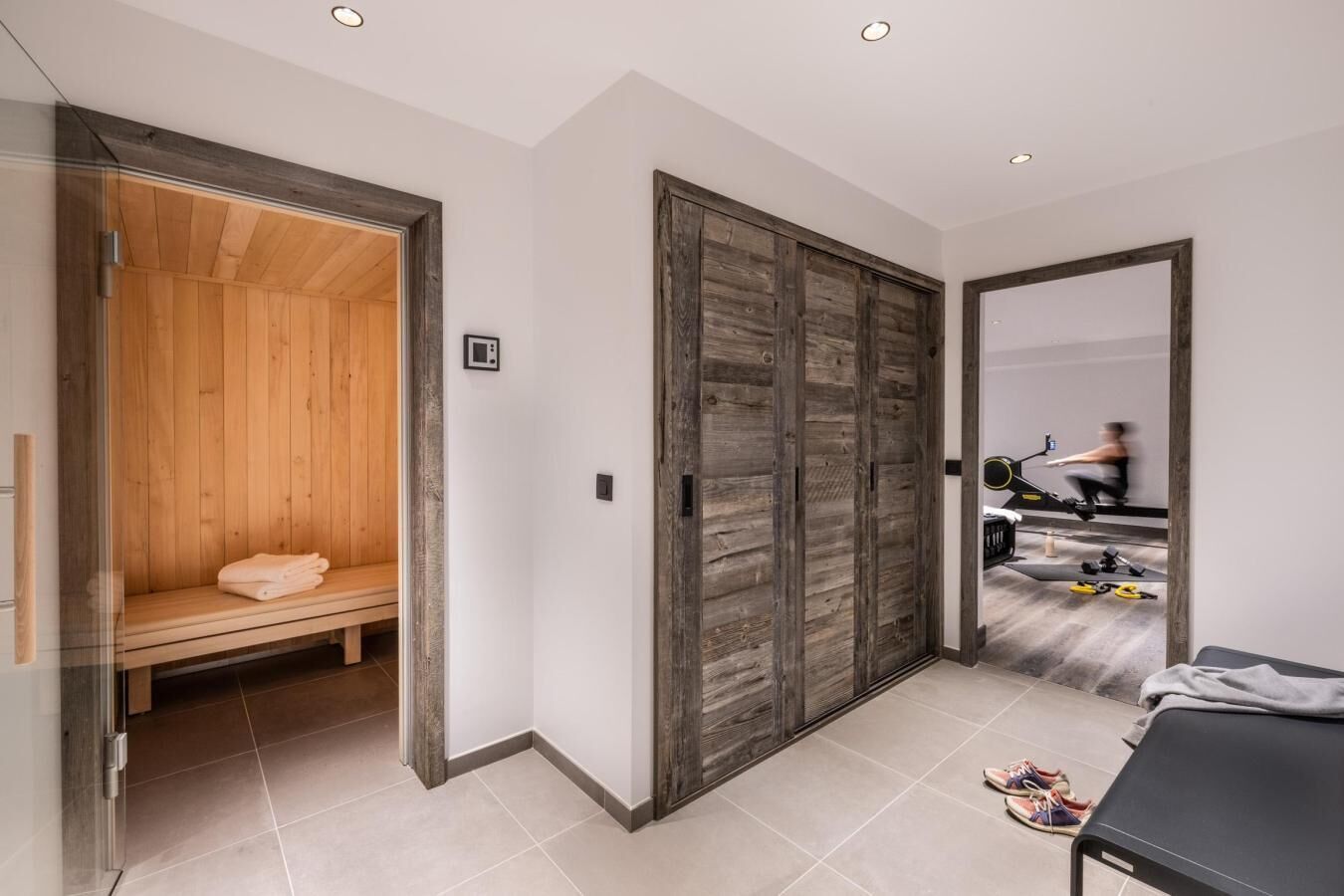 A modern interior with a sauna, exercise equipment, and a bench with towels.
