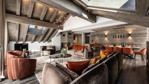 Un vaste espace de vie doté d’un haut plafond, de poutres apparentes et d’une cheminée. On y trouve plusieurs coins salon avec des canapés et des fauteuils.