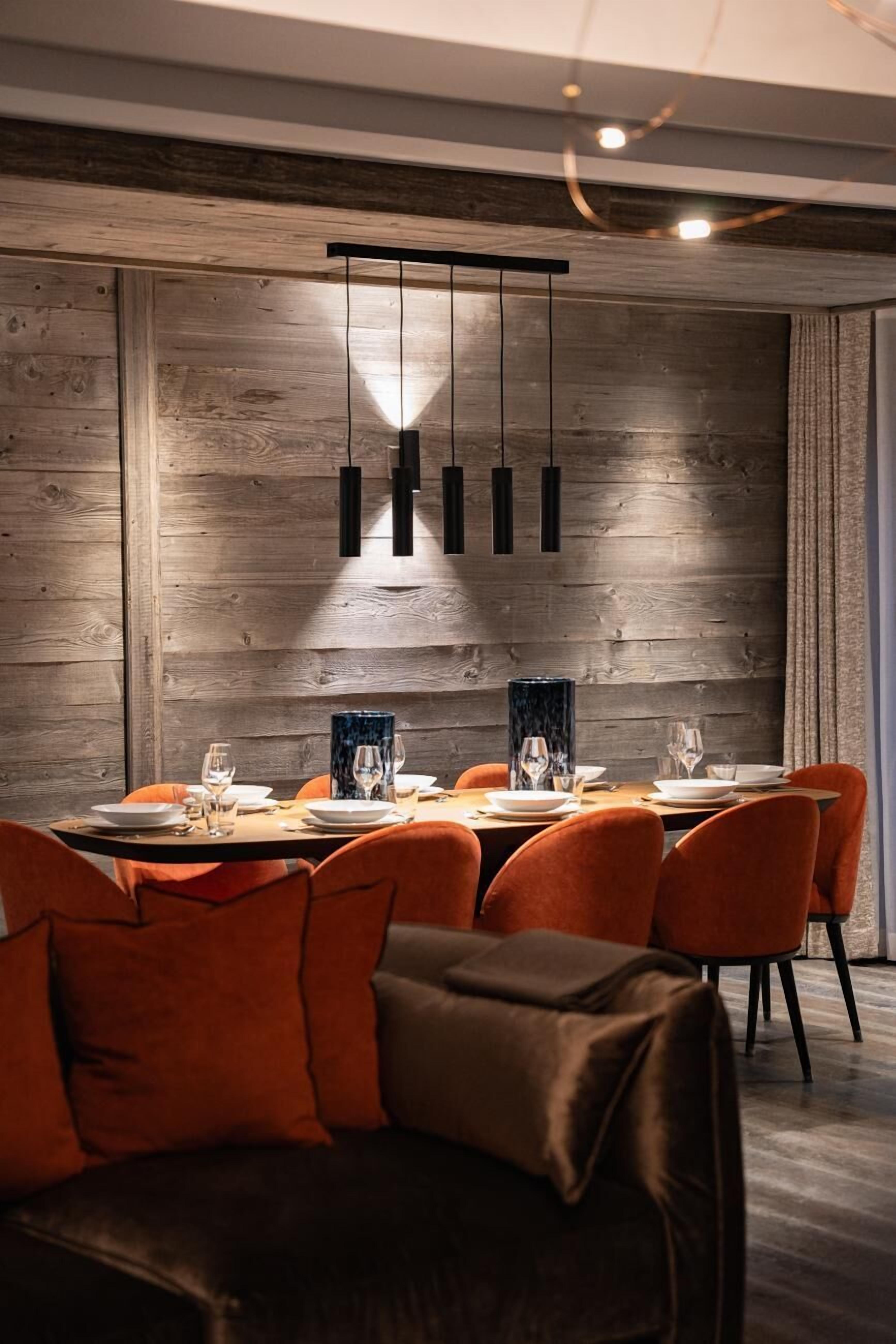 A modern dining area with a wooden wall, a round table set for six, and orange chairs.