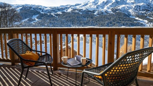 Une terrasse en bois avec deux chaises et une table, offrant une vue sur un paysage montagneux enneigé.