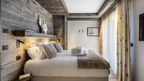 Une chambre à coucher avec une tête de lit en bois, un lit recouvert de draps blancs, une tête de cerf accrochée au mur et une table de chevet sur laquelle repose un livre.