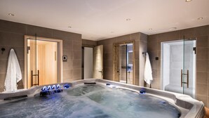 Una moderna spa con una grande vasca idromassaggio, cabine doccia in vetro e una porta in legno che dà su un'altra stanza.