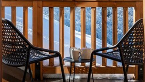 Un pontile di legno con due sedie e un tavolo, affacciato su una montagna e una foresta innevate.