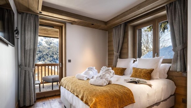 A bedroom with a large bed, a wooden ceiling, and a view of a snowy landscape through a window. - Wifi, 150m from ski slopes, 1st floor, view mountain, sauna, hammam, balcony, fireplace or stove, tv (Méribel - Les Allues)